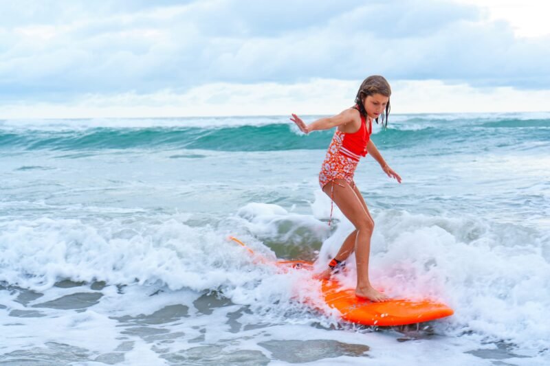 A young girl riding a wave on an orange surfboard in the ocean.
