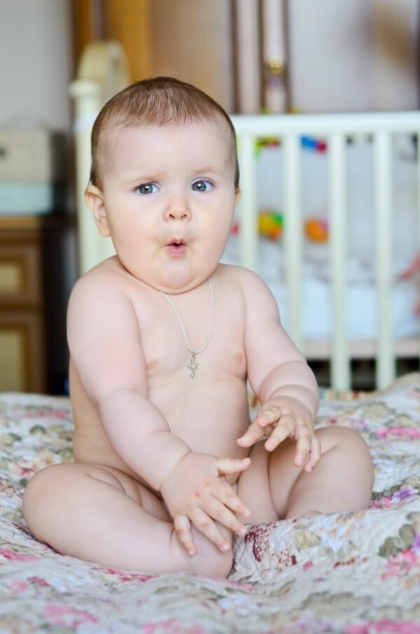Chubby baby sitting on a floral blanket with a surprised facial expression, making a funny mouth shape