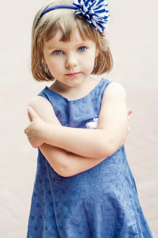 Portrait of a little girl with blue eyes and short hair wearing a blue dress and a large flower headband