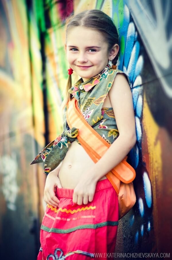 Smiling young girl in stylish bohemian clothes leaning against a bright graffiti wall