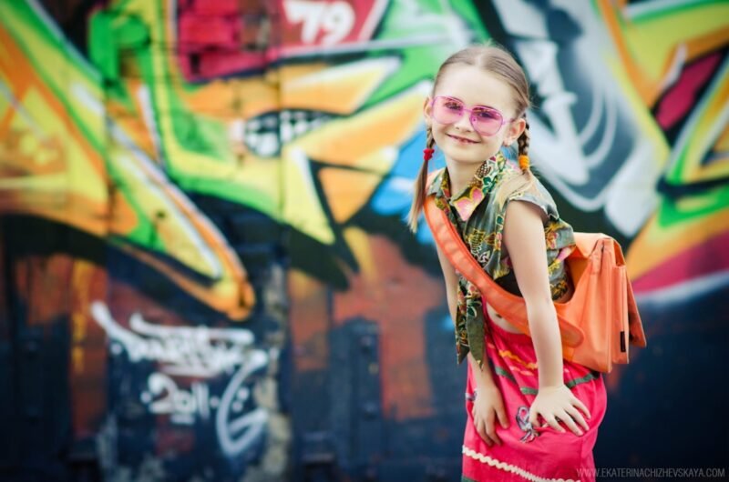 Happy young girl with pigtails and sunglasses posing in front of a street art graffiti background