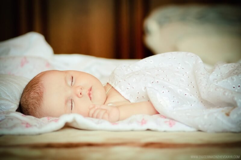 Peaceful newborn baby sleeping soundly in a crib under a white eyelet blanket