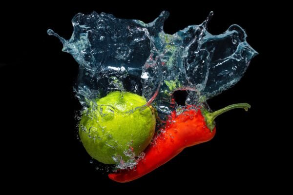 A fresh green lime and a red chili pepper splashing into water with bubbles against a black background