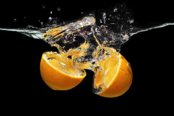 Two orange halves sinking in water with a large splash and crystal clear ripples against a black background