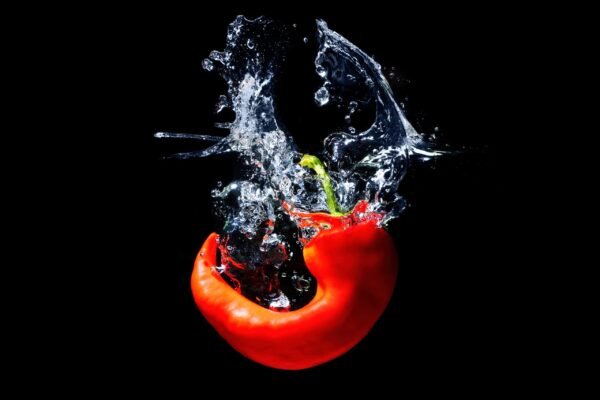 Red bell pepper dropping into water with a dynamic splash and air bubbles on a solid black background