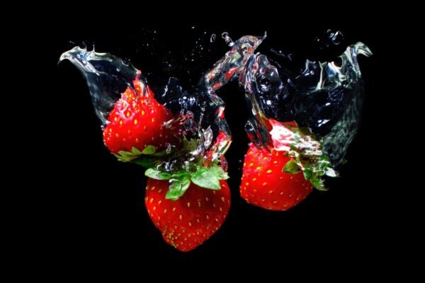 Three ripe red strawberries falling into water with dramatic high speed splashes against a black background