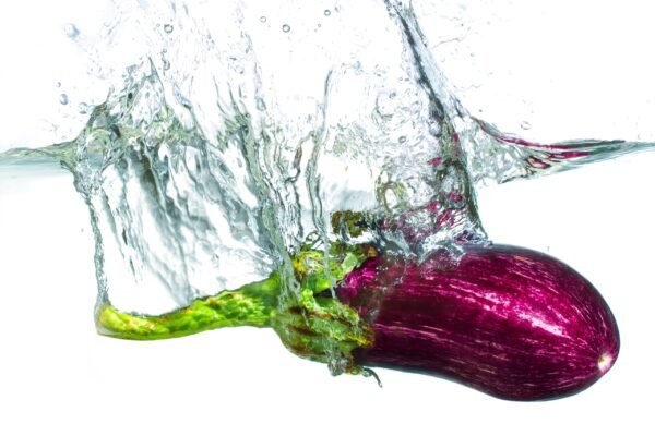 A striped eggplant fully submerged in water with a large, dramatic splash and air bubbles