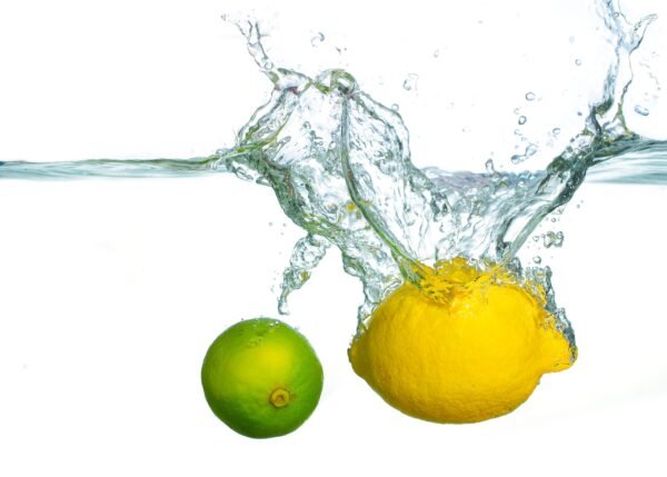 A fresh yellow lemon and a green lime splashing into clean water against a white background
