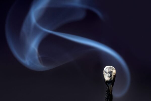 Macro shot of a burnt match head with a swirling, artistic pattern of blue smoke on a dark background