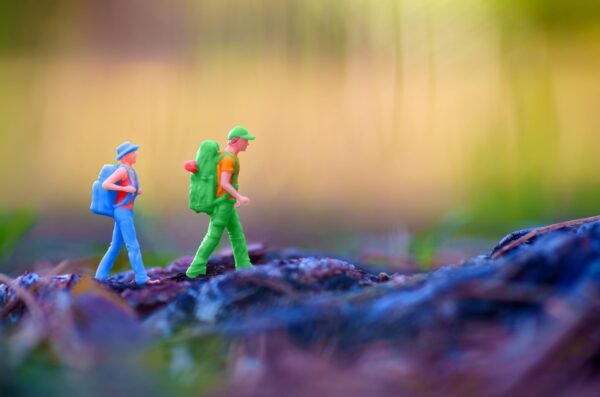 Two miniature hiker figurines with backpacks trekking over a rough rocky surface with a blurred natural background