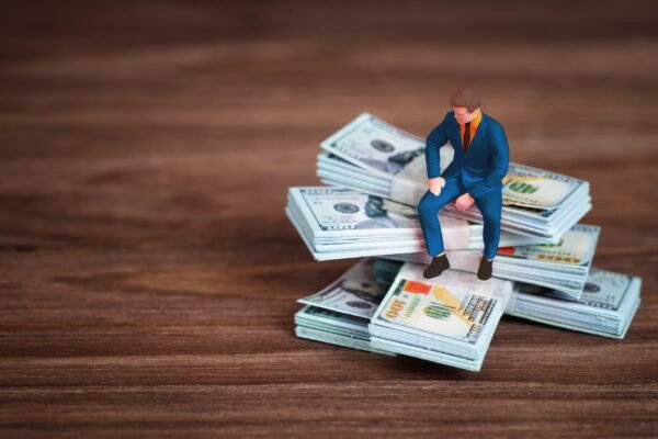 Miniature businessman figure sitting on a stack of US one hundred dollar bills on a wooden surface