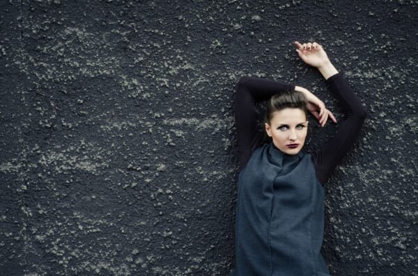 High fashion portrait of a woman with dramatic makeup posing against a dark textured concrete wall