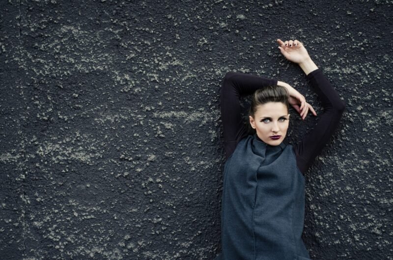 High fashion portrait of a woman with dramatic makeup posing against a dark textured concrete wall