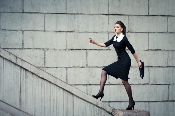 Elegant woman in a black dress with a white lace collar walking up concrete stairs in an urban setting