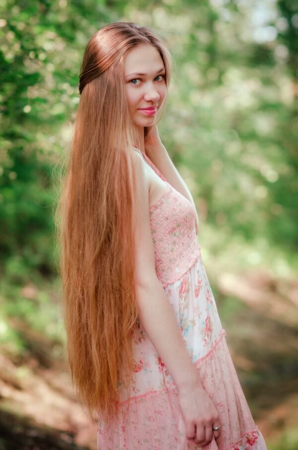 Side profile of a young woman with long hair looking over her shoulder in a sunlit forest background