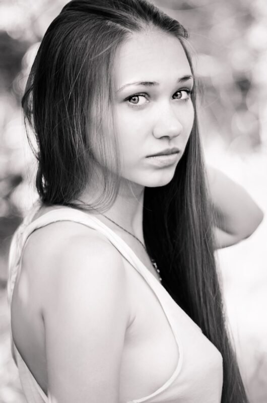 Black and white portrait of a young woman with long hair looking over her shoulder outdoors