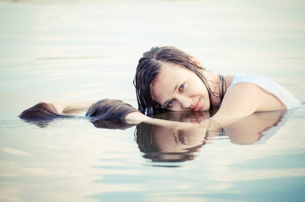 Young woman floating in calm water with her reflection visible on the surface