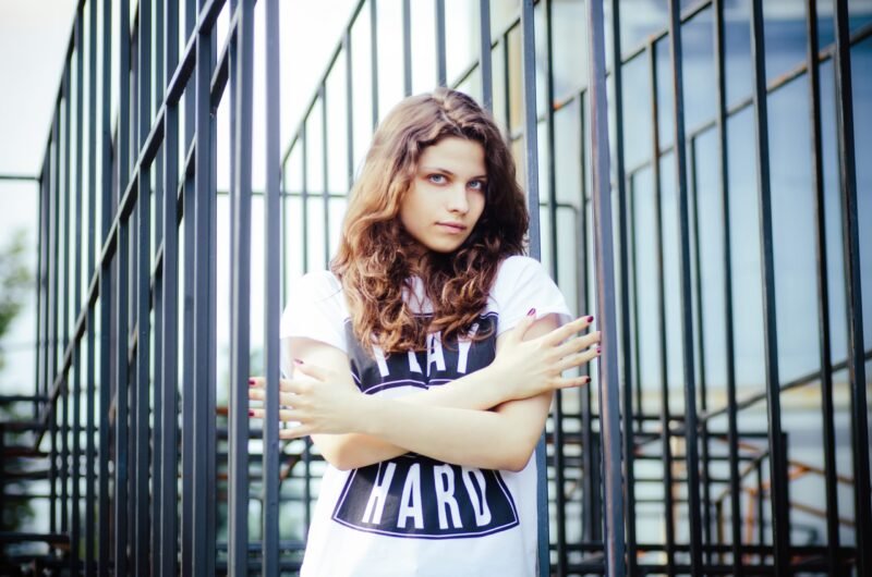 Young woman with curly hair standing behind a black metal fence structure