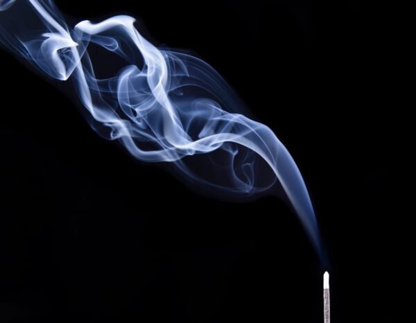 Wispy white incense smoke drifting diagonally upwards from a glowing stick on a black background